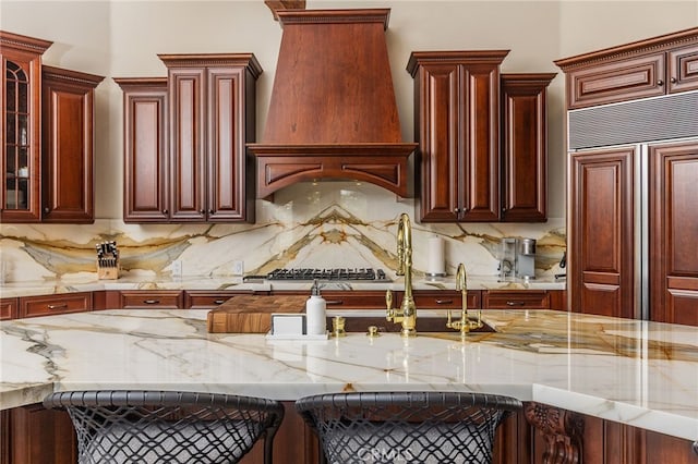 kitchen featuring premium range hood, reddish brown cabinets, light stone countertops, and stainless steel gas cooktop