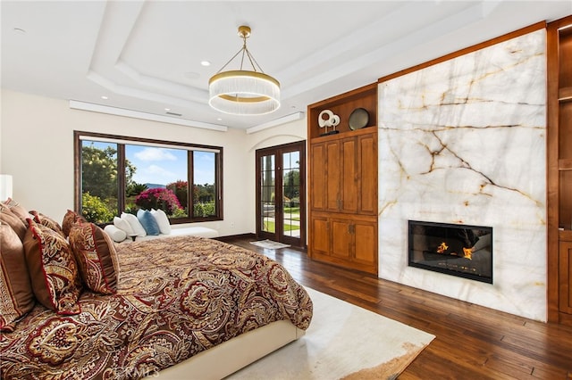 bedroom with a premium fireplace, dark wood-type flooring, a tray ceiling, and access to outside