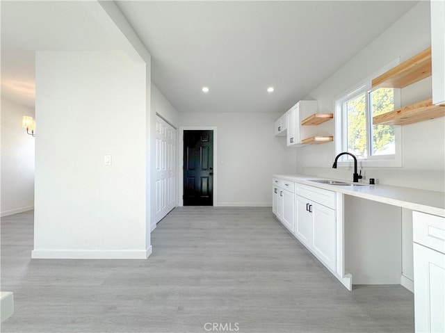 kitchen with a sink, open shelves, white cabinetry, and light countertops