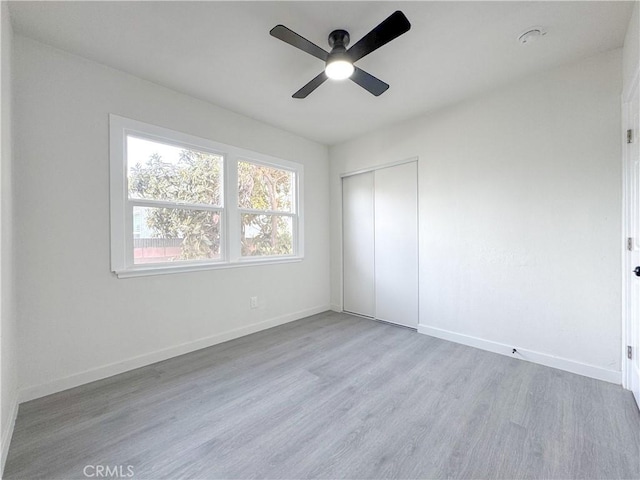 unfurnished bedroom featuring ceiling fan, a closet, baseboards, and wood finished floors