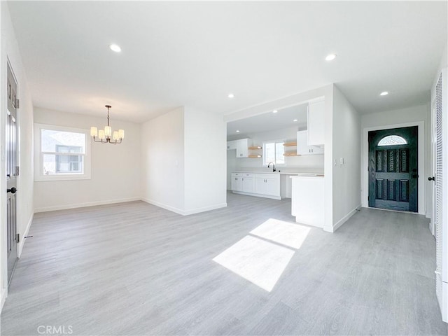 unfurnished living room with an inviting chandelier, recessed lighting, light wood-style floors, and baseboards