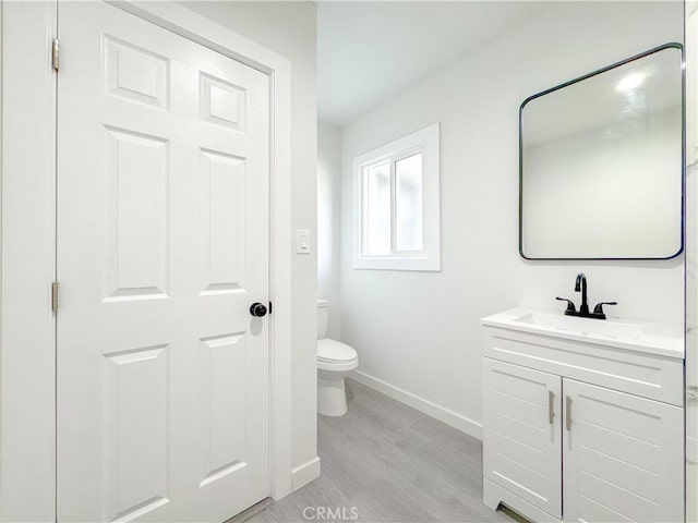 bathroom with vanity, toilet, wood finished floors, and baseboards