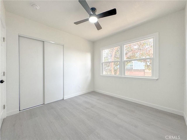 unfurnished bedroom with light wood finished floors, a closet, baseboards, and a ceiling fan