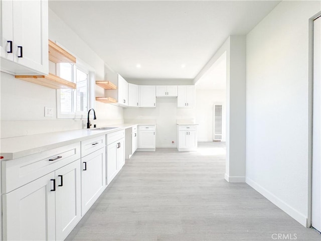 kitchen with a sink, light wood-type flooring, baseboards, and white cabinets