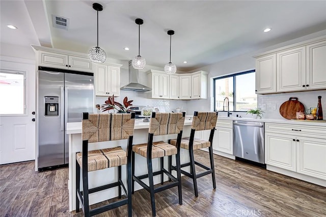 kitchen with dark wood-type flooring, wall chimney range hood, visible vents, and appliances with stainless steel finishes