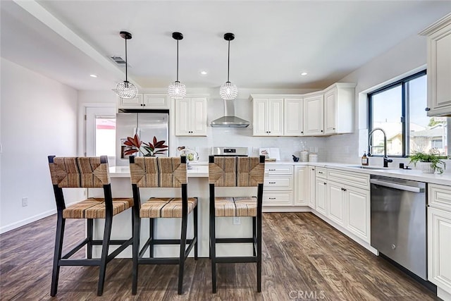 kitchen featuring wall chimney range hood, a kitchen breakfast bar, dark wood-style floors, stainless steel appliances, and a sink