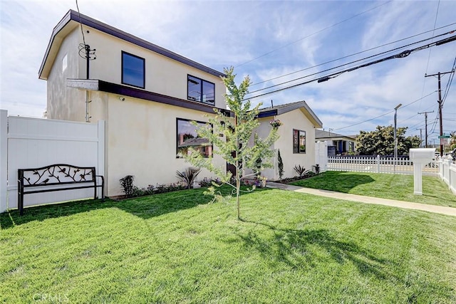 back of house with stucco siding, a yard, and fence