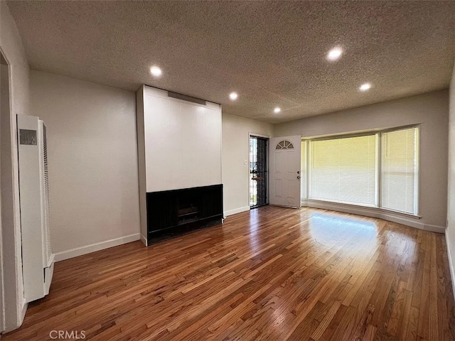 unfurnished living room featuring wood finished floors, recessed lighting, a fireplace, baseboards, and a heating unit