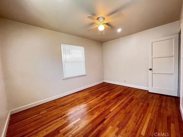 spare room with baseboards, dark wood-style flooring, and a ceiling fan