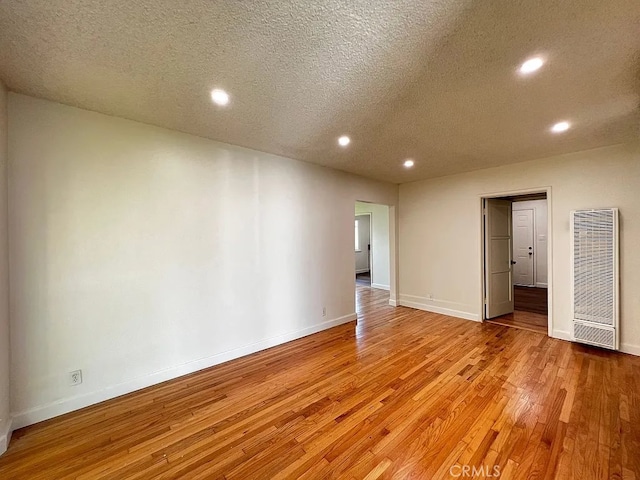 spare room featuring baseboards, light wood finished floors, recessed lighting, a heating unit, and a textured ceiling