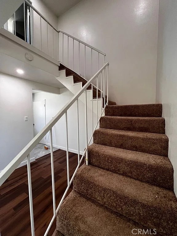 stairway featuring a high ceiling, baseboards, and wood finished floors