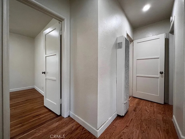 corridor with baseboards, wood finished floors, and a heating unit