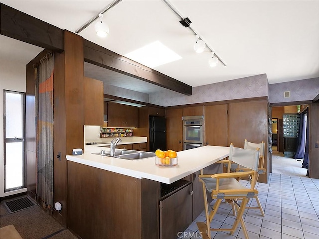 kitchen featuring a peninsula, freestanding refrigerator, a sink, light countertops, and double oven