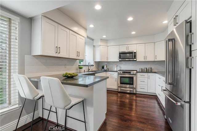 kitchen featuring a sink, dark countertops, dark wood-style floors, appliances with stainless steel finishes, and a peninsula