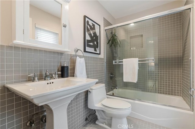 bathroom with toilet, a sink, tile walls, tile patterned flooring, and bath / shower combo with glass door