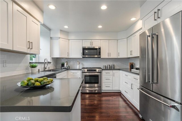 kitchen with dark wood-style floors, a sink, stainless steel appliances, white cabinetry, and dark countertops