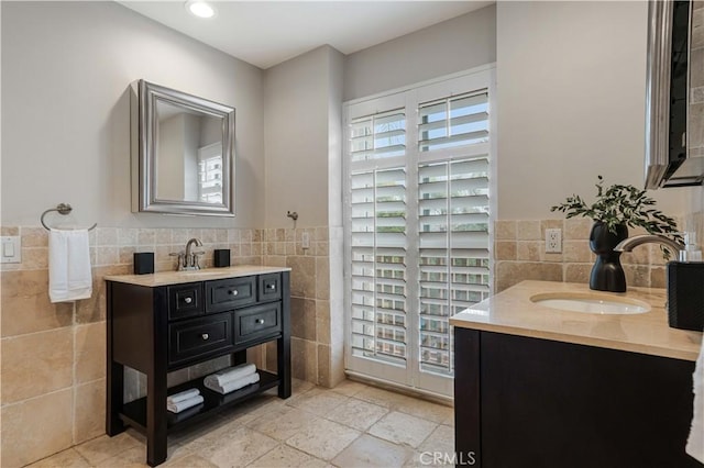 bathroom featuring a sink, two vanities, tile walls, and wainscoting