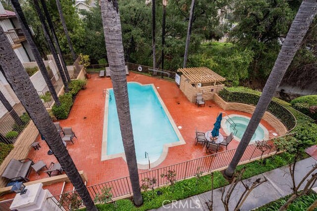 community pool with a patio area, a community hot tub, an outdoor structure, and fence