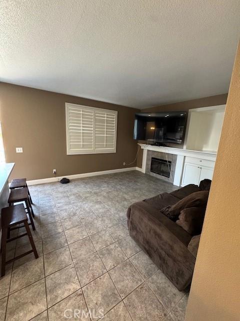 living area featuring tile patterned floors, baseboards, a textured ceiling, and a tiled fireplace