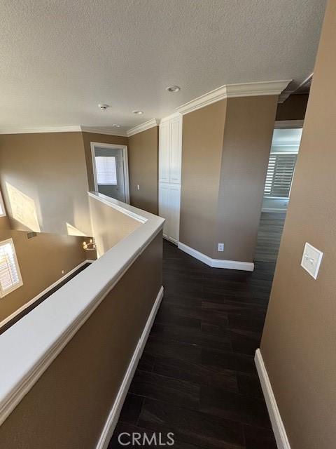 corridor featuring baseboards, a textured ceiling, dark wood finished floors, and ornamental molding