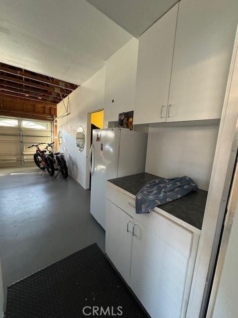 kitchen with dark countertops, finished concrete floors, white cabinetry, and freestanding refrigerator