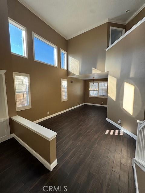 unfurnished living room with crown molding, baseboards, dark wood-type flooring, and a towering ceiling