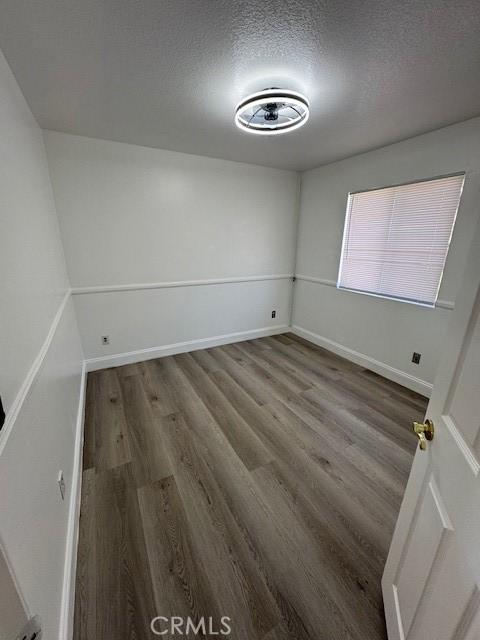 empty room with a textured ceiling, baseboards, and wood finished floors