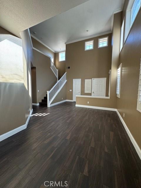 unfurnished living room with wood finished floors, baseboards, and ornamental molding