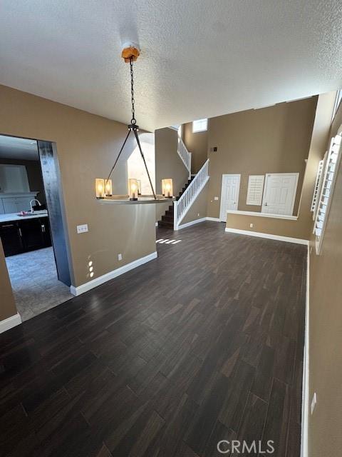 unfurnished living room with dark wood-type flooring, a sink, a textured ceiling, stairway, and a chandelier