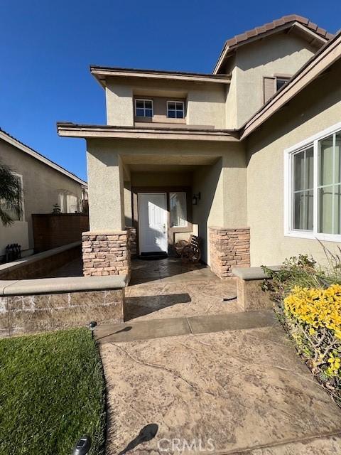 entrance to property featuring stucco siding, stone siding, a patio, and fence