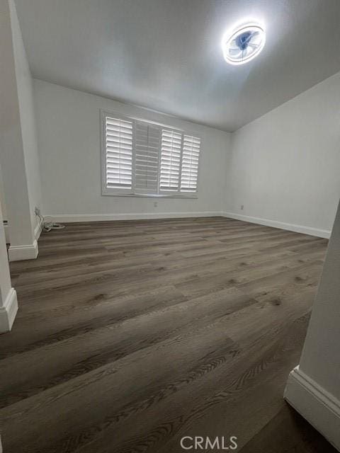 unfurnished room featuring dark wood finished floors, lofted ceiling, and baseboards