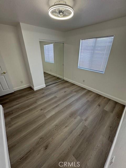 unfurnished bedroom featuring a closet, a textured ceiling, baseboards, and wood finished floors