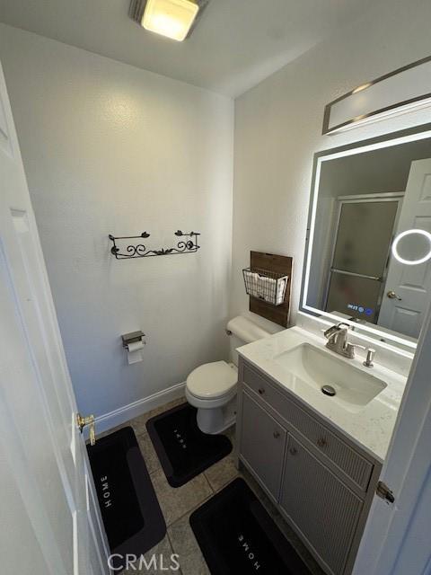 bathroom featuring tile patterned flooring, a shower with door, baseboards, toilet, and vanity