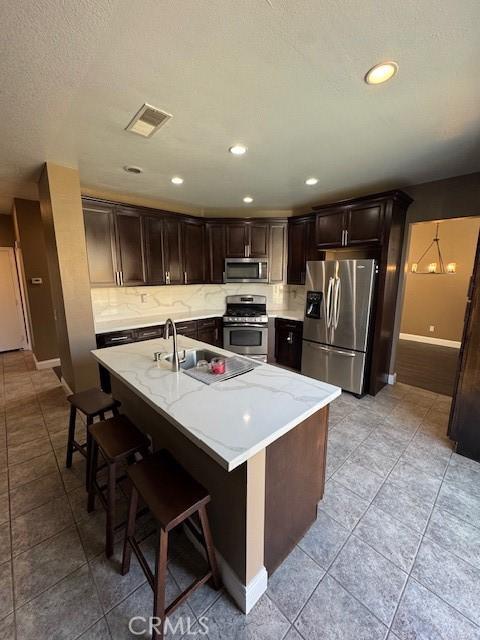 kitchen with visible vents, a sink, stainless steel appliances, dark brown cabinets, and backsplash