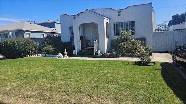 mediterranean / spanish-style house featuring stucco siding, a front lawn, and fence