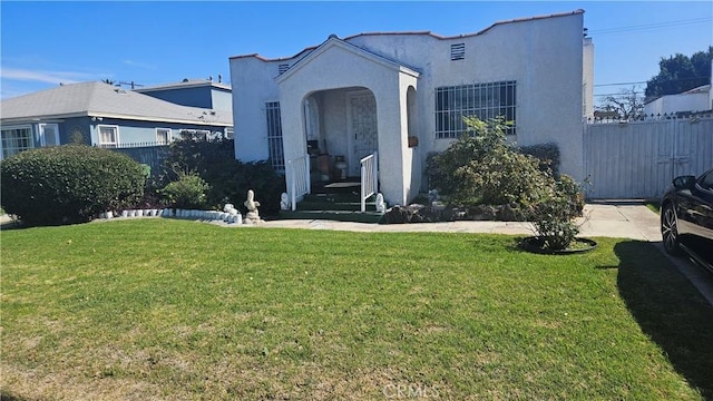 mediterranean / spanish-style house featuring stucco siding, a front lawn, and fence