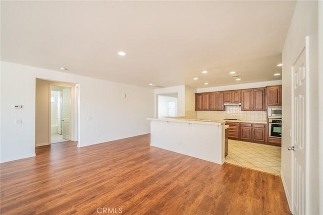 kitchen featuring open floor plan, light countertops, under cabinet range hood, light wood finished floors, and appliances with stainless steel finishes