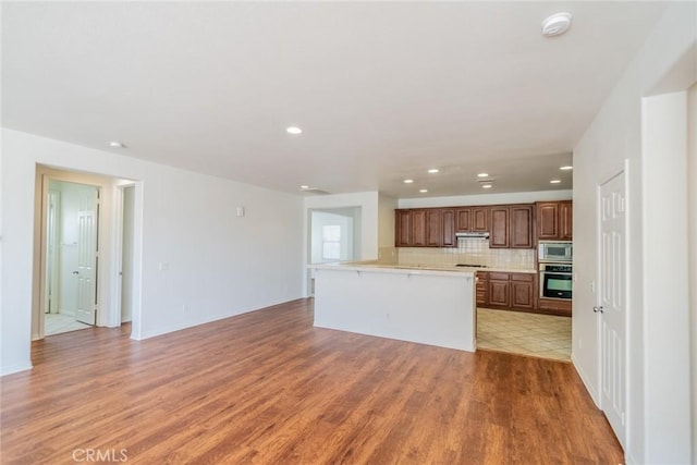 kitchen with light countertops, light wood finished floors, appliances with stainless steel finishes, under cabinet range hood, and decorative backsplash
