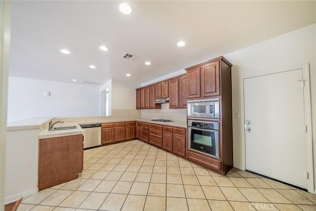 kitchen featuring a sink, backsplash, appliances with stainless steel finishes, a peninsula, and visible vents