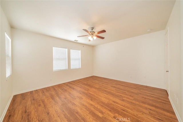unfurnished room featuring baseboards, visible vents, wood finished floors, and a ceiling fan