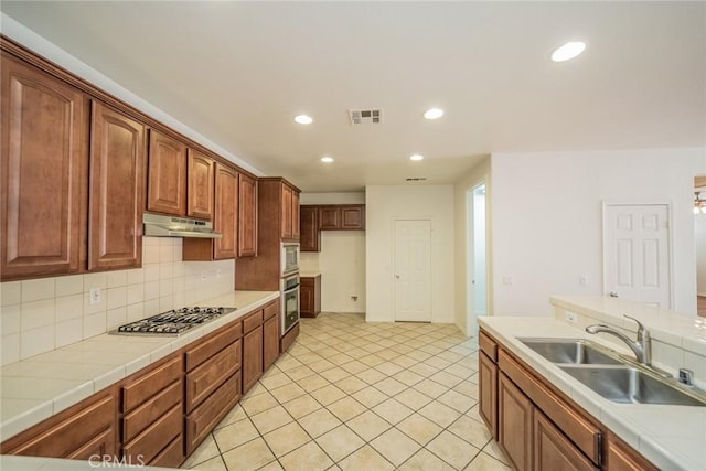 kitchen featuring a sink, under cabinet range hood, stainless steel appliances, tile countertops, and visible vents