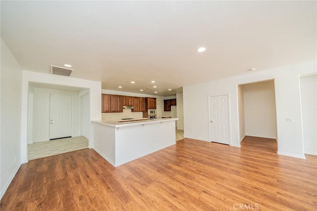 kitchen with light countertops, light wood-style flooring, visible vents, a peninsula, and under cabinet range hood