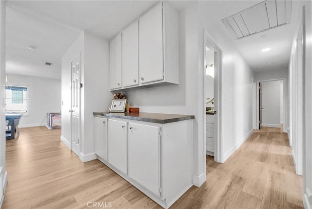 corridor featuring visible vents, attic access, light wood-type flooring, and baseboards