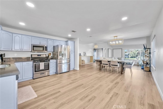 kitchen with a sink, dark countertops, light wood-style floors, and appliances with stainless steel finishes