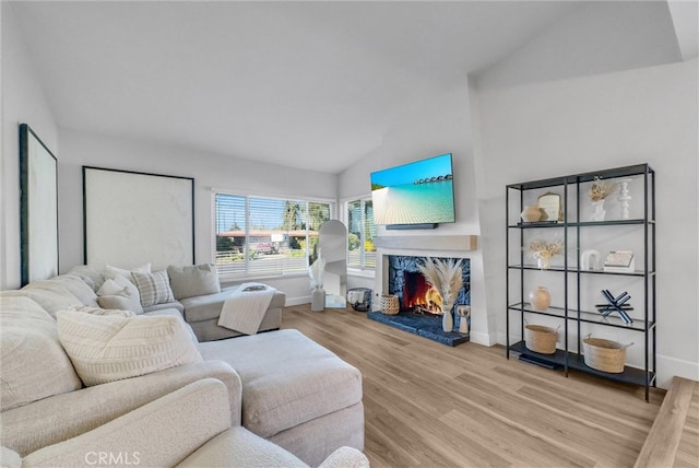 living area featuring baseboards, a warm lit fireplace, wood finished floors, and vaulted ceiling