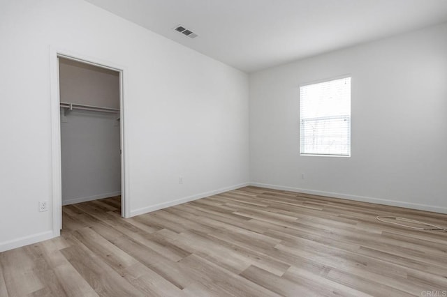 unfurnished bedroom with light wood-type flooring, visible vents, baseboards, and a walk in closet