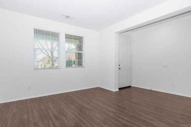 empty room with visible vents, baseboards, and dark wood-style flooring