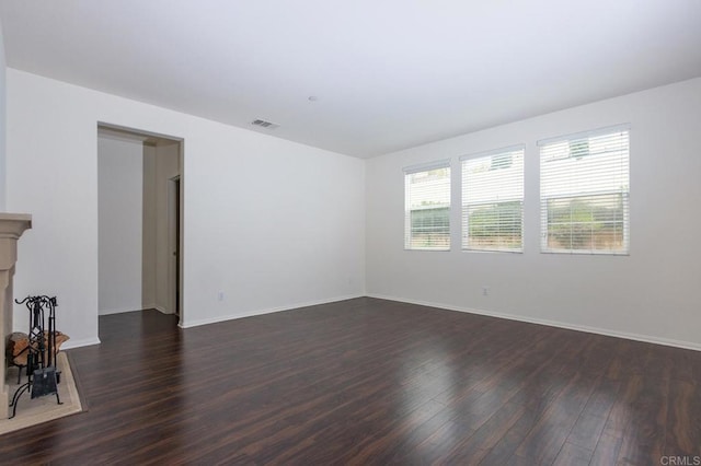 spare room with visible vents, baseboards, a fireplace with raised hearth, and dark wood-style floors