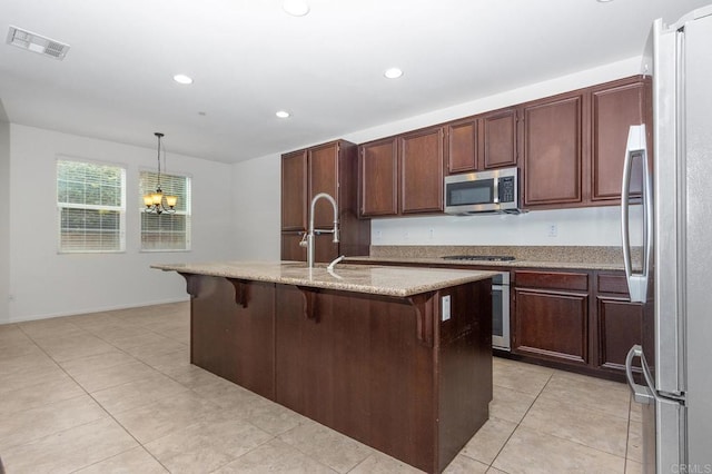 kitchen with visible vents, a kitchen island with sink, a sink, appliances with stainless steel finishes, and pendant lighting