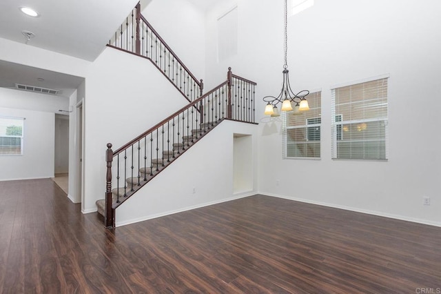 stairs with an inviting chandelier, wood finished floors, visible vents, and a towering ceiling